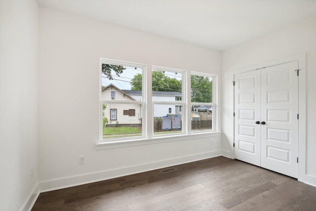 unfurnished room with dark wood-type flooring, visible vents, and baseboards