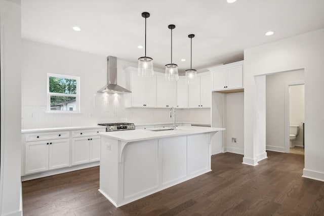 kitchen with a kitchen island with sink, light countertops, a sink, and wall chimney range hood