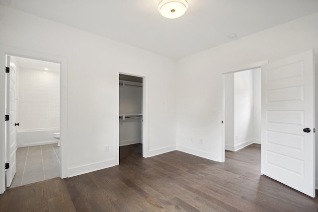 unfurnished bedroom with dark wood-type flooring, a closet, ensuite bath, and baseboards