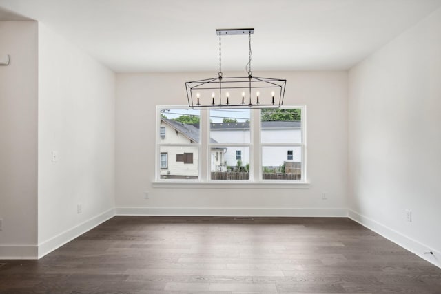 unfurnished dining area featuring a chandelier, dark wood-type flooring, and baseboards