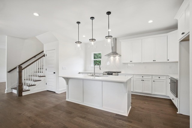 kitchen featuring light countertops, wall chimney range hood, a sink, and a center island with sink