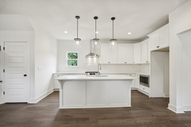 kitchen featuring light countertops, stainless steel microwave, white cabinetry, a sink, and an island with sink