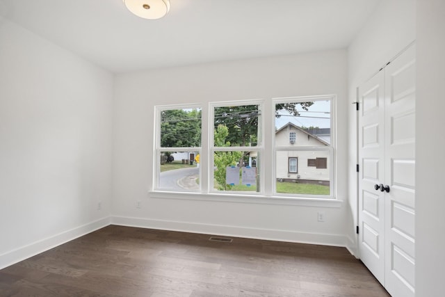 spare room with dark wood-style floors, visible vents, and baseboards