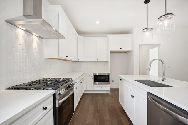 kitchen featuring wall chimney range hood, appliances with stainless steel finishes, light countertops, and a sink