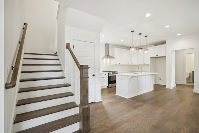 kitchen with light countertops, a kitchen island with sink, white cabinetry, wall chimney range hood, and stainless steel gas range oven