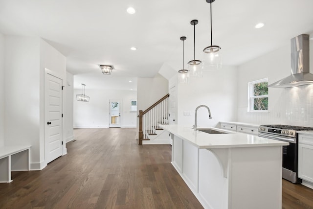 kitchen with an island with sink, gas range, wall chimney exhaust hood, decorative light fixtures, and a sink