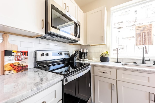 kitchen featuring white cabinets, decorative backsplash, light stone counters, stainless steel appliances, and a sink