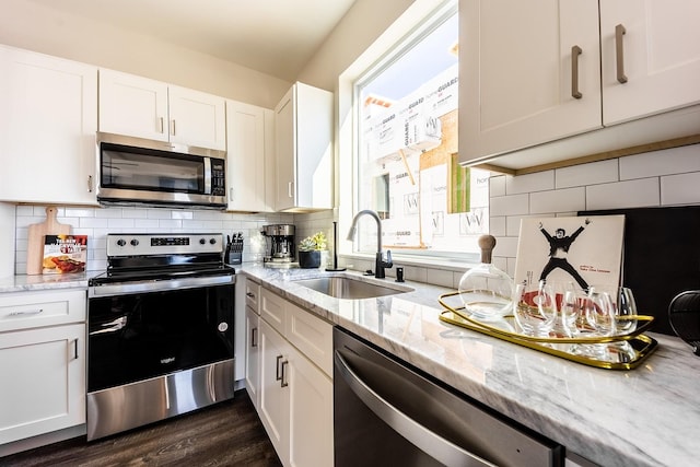 kitchen with white cabinets, decorative backsplash, light stone counters, stainless steel appliances, and a sink