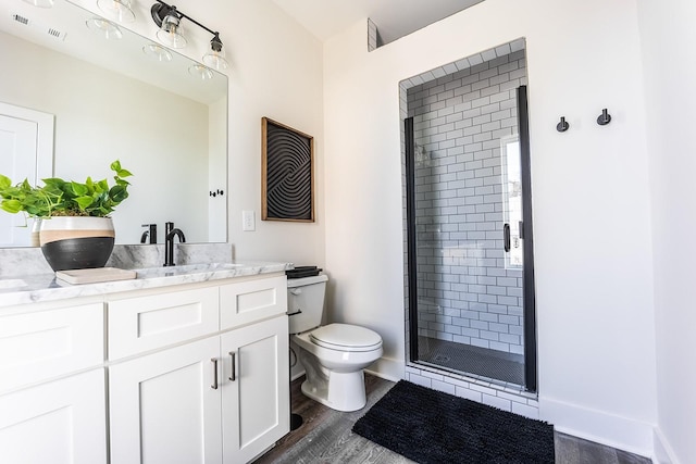 bathroom featuring baseboards, toilet, wood finished floors, vanity, and a shower stall