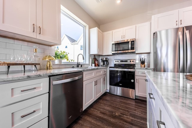 kitchen with tasteful backsplash, white cabinets, light stone counters, stainless steel appliances, and a sink