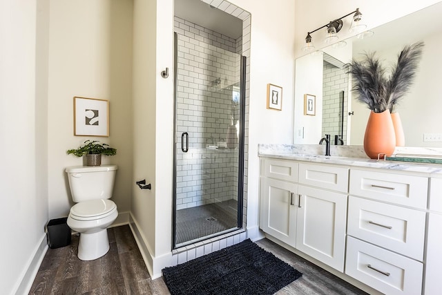 bathroom with toilet, a stall shower, wood finished floors, and vanity