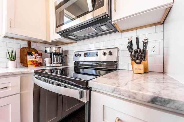 kitchen with light stone countertops, white cabinetry, stainless steel appliances, and backsplash