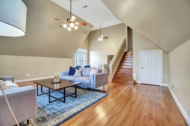 living area featuring light wood finished floors, baseboards, a ceiling fan, lofted ceiling, and stairs