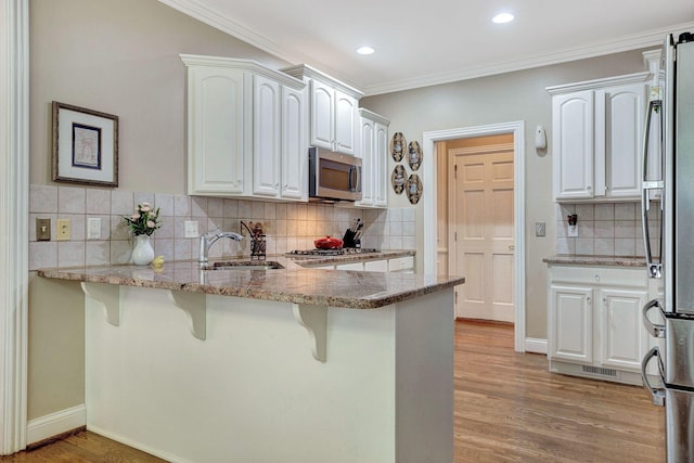 kitchen featuring appliances with stainless steel finishes, light wood-style floors, white cabinets, a sink, and a peninsula