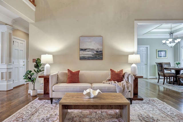 living room with decorative columns, baseboards, ornamental molding, wood finished floors, and an inviting chandelier