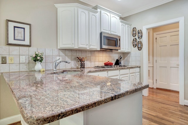 kitchen featuring stainless steel appliances, a peninsula, a sink, white cabinetry, and light stone countertops