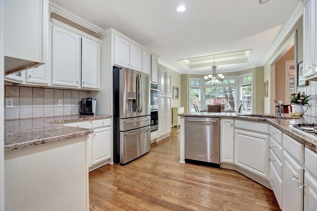 kitchen featuring light wood finished floors, white cabinets, a peninsula, a tray ceiling, and stainless steel appliances