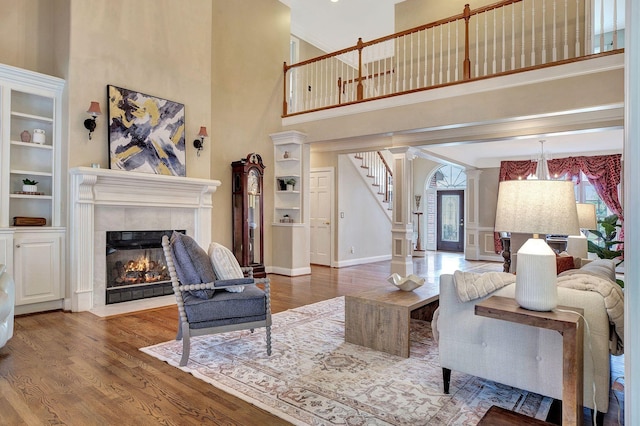 living area with ornate columns, a fireplace, stairway, and wood finished floors