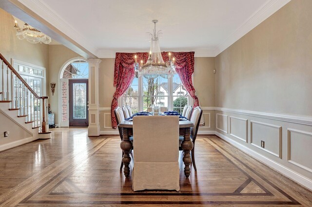 dining area featuring an inviting chandelier, ornamental molding, a decorative wall, and ornate columns