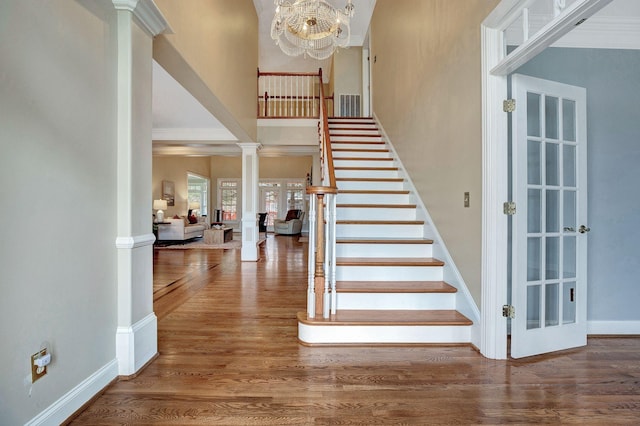 stairway featuring crown molding, ornate columns, a towering ceiling, wood finished floors, and baseboards