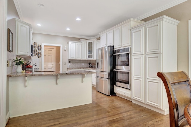 kitchen featuring light wood-style flooring, stainless steel appliances, a peninsula, light stone countertops, and a kitchen bar