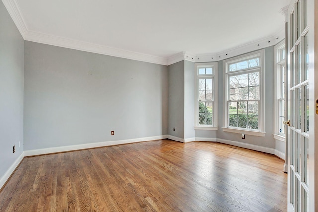 spare room with crown molding, baseboards, and wood finished floors