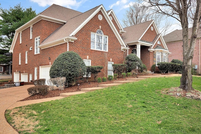 traditional-style home with brick siding, an attached garage, a shingled roof, and a front yard