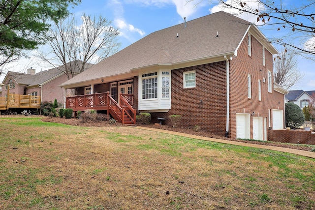 rear view of property with a garage, a shingled roof, a lawn, a deck, and brick siding