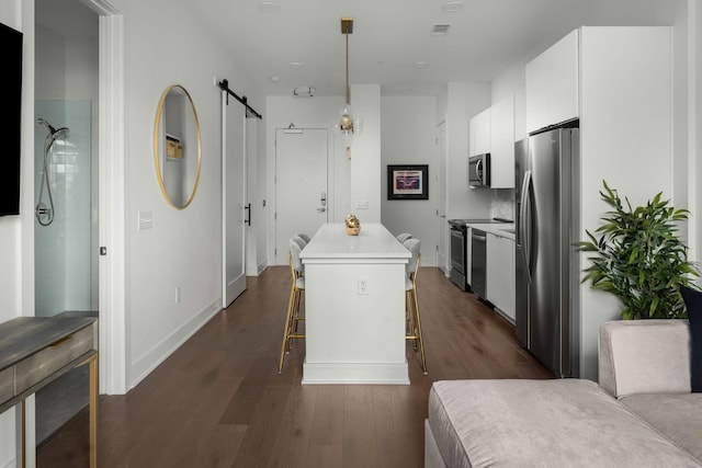 kitchen with a barn door, a kitchen island, appliances with stainless steel finishes, a breakfast bar area, and white cabinetry