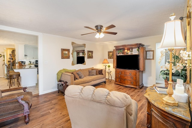 living area featuring a ceiling fan, crown molding, light wood-style flooring, and baseboards