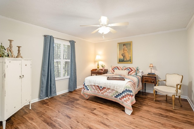 bedroom with crown molding, visible vents, baseboards, and wood finished floors