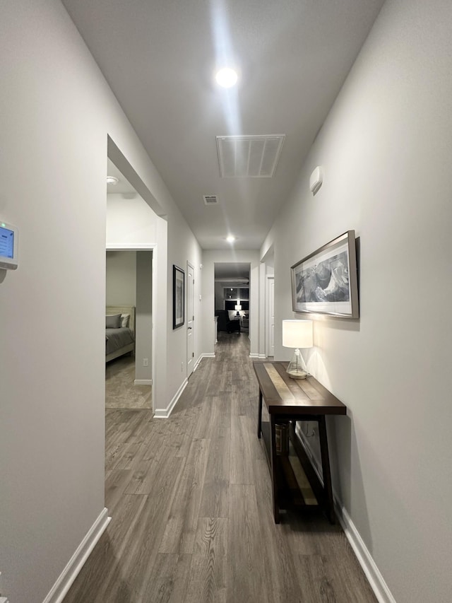 hall featuring baseboards, visible vents, and wood finished floors