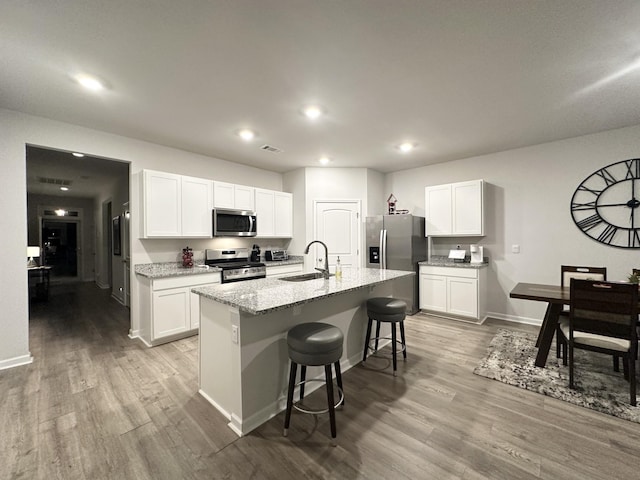 kitchen featuring a sink, white cabinets, appliances with stainless steel finishes, light stone countertops, and an island with sink