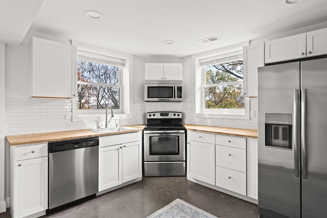 kitchen featuring stainless steel appliances, a sink, wooden counters, and white cabinetry