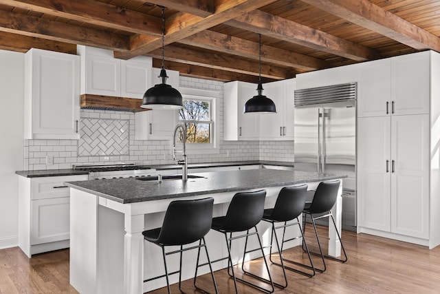 kitchen featuring built in refrigerator, a kitchen island with sink, white cabinetry, and pendant lighting