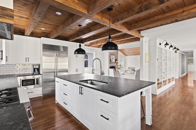 kitchen featuring an island with sink, built in appliances, white cabinetry, pendant lighting, and a sink