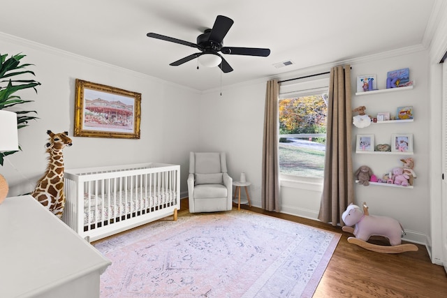 bedroom featuring a crib, visible vents, crown molding, and wood finished floors