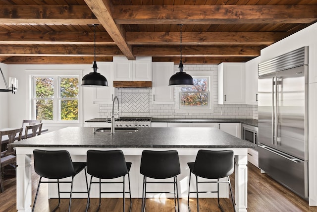 kitchen featuring pendant lighting, decorative backsplash, white cabinetry, an island with sink, and built in refrigerator