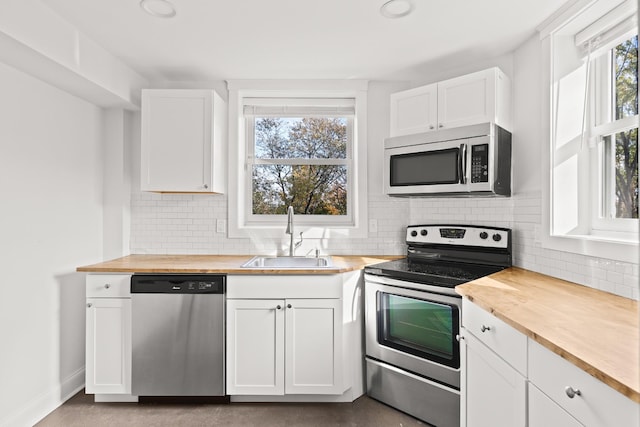 kitchen with stainless steel appliances, a sink, white cabinets, wooden counters, and a wealth of natural light