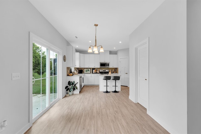 kitchen featuring decorative light fixtures, light countertops, appliances with stainless steel finishes, white cabinets, and a kitchen island