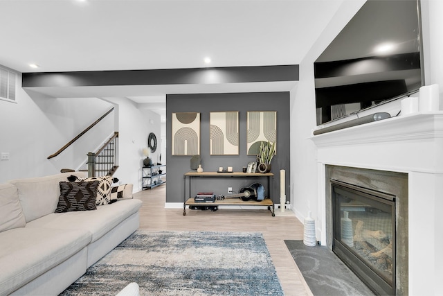 living room with a fireplace with flush hearth, baseboards, light wood finished floors, and stairs