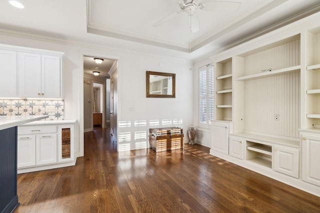 interior space with built in features, ceiling fan, dark wood-type flooring, a tray ceiling, and crown molding