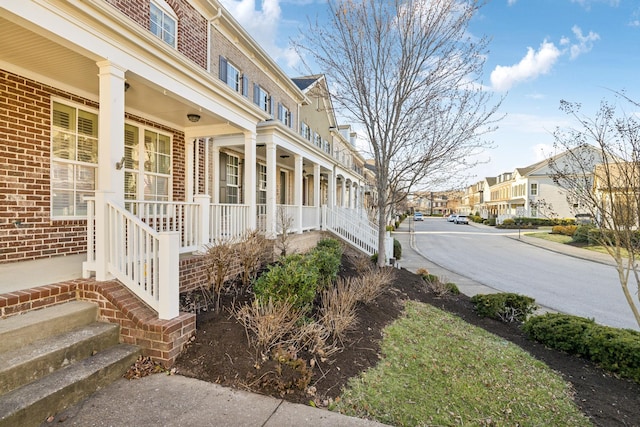 view of property exterior featuring a residential view, a porch, and brick siding