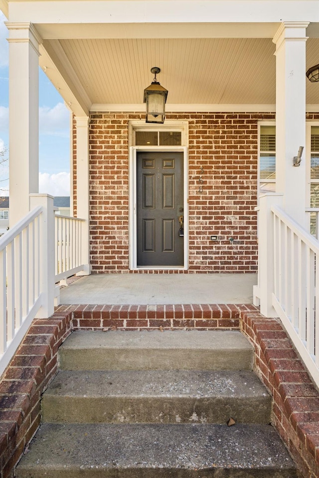 view of exterior entry featuring brick siding and a porch