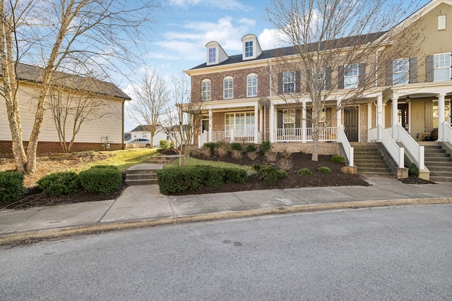 view of front of house featuring covered porch, stairway, and brick siding