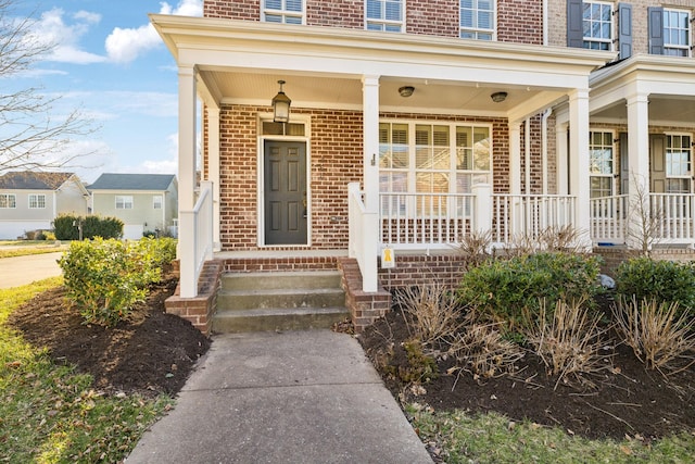 view of exterior entry featuring brick siding and a porch