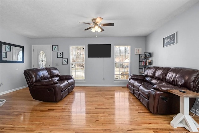 living area with light wood-style flooring, a textured ceiling, baseboards, and a ceiling fan