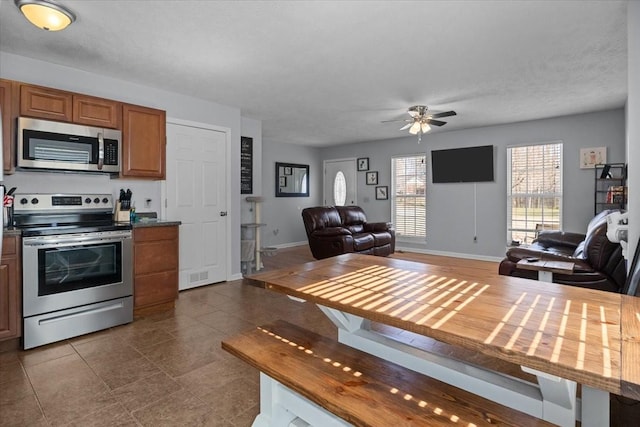 kitchen featuring stainless steel appliances, dark countertops, brown cabinetry, open floor plan, and baseboards