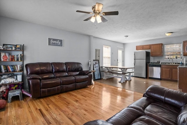 living room with ceiling fan, light wood-style flooring, and a textured ceiling