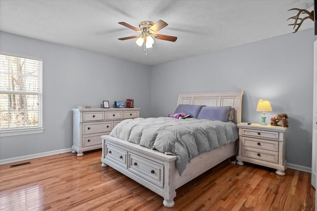 bedroom with baseboards, a ceiling fan, visible vents, and light wood-style floors